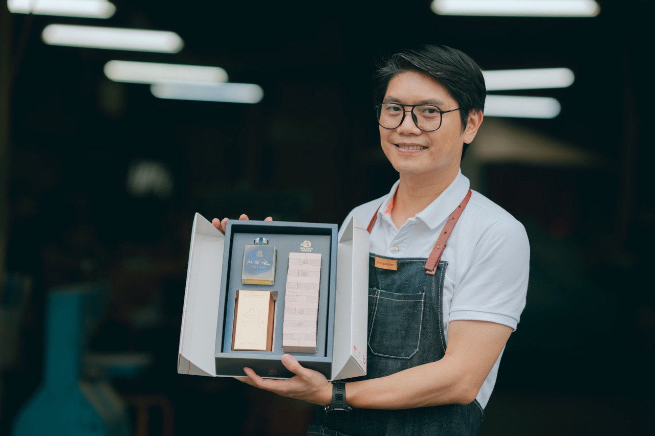 周信宏手持與第 62 屆金馬獎合作推出的聯名禮盒。以「聚在一起」為主題，結合米香、白蘭地與木作遊戲，象徵影人聚首與永續精神的延續。